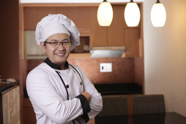 Portrait of happy proud Asian chef smiling at camera with crossed arms, chef in kitchen, successful chef in restaurant business